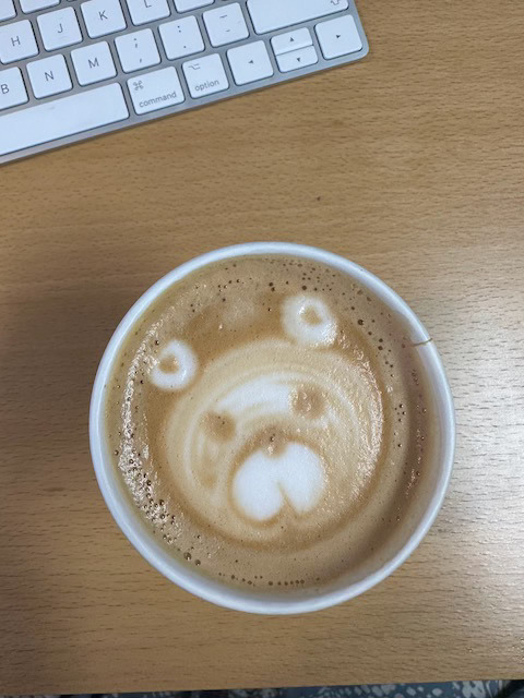 Cappuccino med bamsefjes i melkeskummet på en pult med deler av et tastaur i bildet.