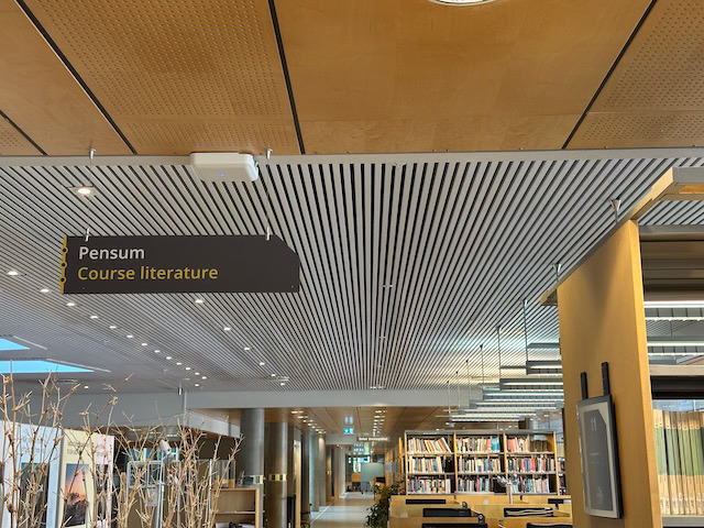 Interiør fra bibliotek med bokhyller og skilt der det står Pensum Course literature